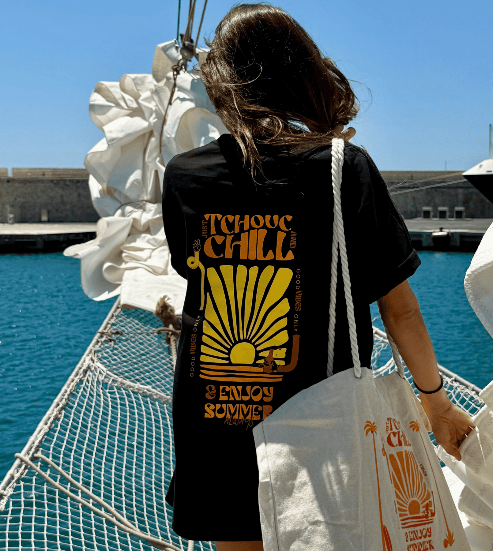 Femme sur un bateau face à la mer portant un tee shirt noir de la marque Tchouc & Chill